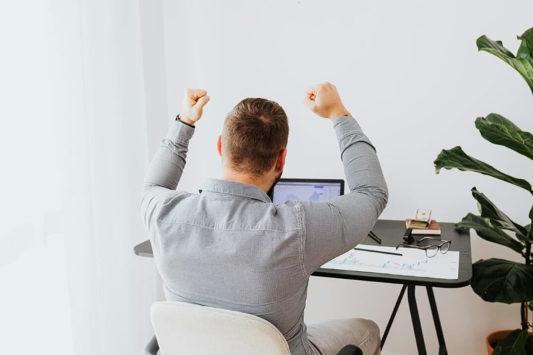 Un dirigeant confiant et dynamique qui lève les bras en signe de victoire devant son ordinateur : image de la performance mentale atteinte grâce à la sophrologie, visualisation positive et gestion du stress avant une réunion importante, telle que je l'accompagne.