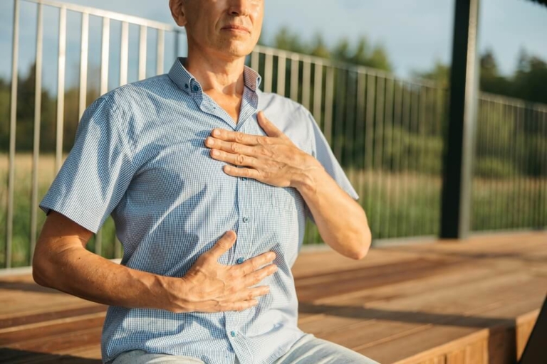 Un homme assis qui pratique une respiration abdominale profonde typique de la sophrologie : mains posées sur le ventre, posture détendue, yeux clos, pour mieux sentir le diaphragme et activer le nerf vague, comme je vous l'enseigne en séance à Vincennes.