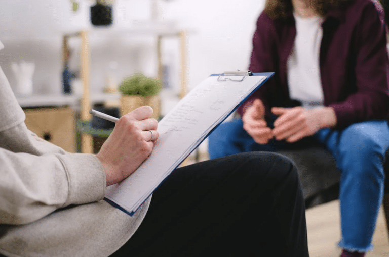 Séance d’accompagnement ou de coaching avec un professionnel prenant des notes sur un clipboard face à un client assis.