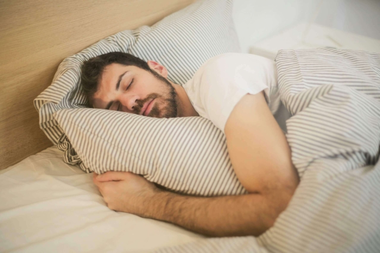 Homme endormi profondément dans un lit confortable, oreiller moelleux et draps clairs, illustration d'un sommeil réparateur favorisé par la sophrologie : respiration calme et relaxation corporelle pour vaincre les insomnies et réveils nocturnes.