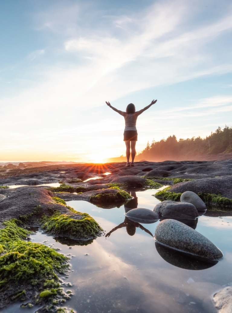 Ressourcement et bien-être en pleine nature avec une femme contemplant le coucher de soleil sur une côte rocheuse